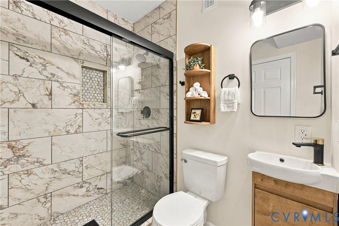 Walk-in shower featuring large-format patterned wall tile, a recessed niche with mosaic tiling, and a sliding glass door with a matte black frame