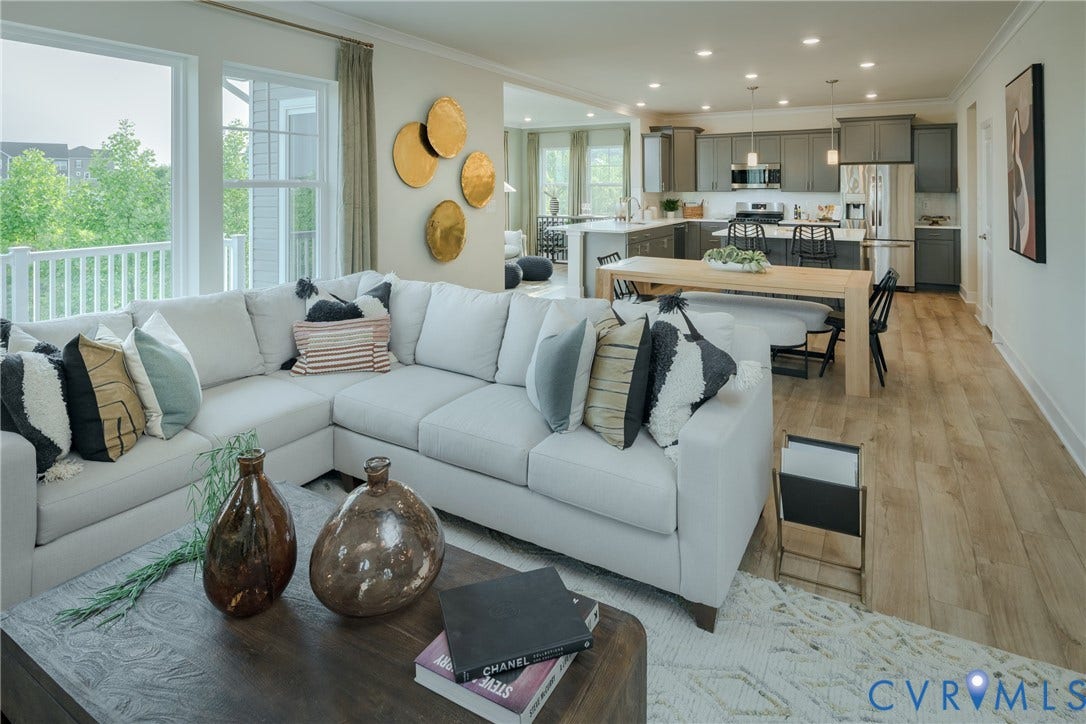 Open-concept living area with wood-finish flooring, a kitchen featuring dark cabinetry and stainless steel appliances, and abundant natural light from large windows
