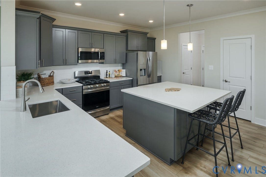 Spacious kitchen featuring gray cabinetry, stainless steel appliances, light-toned countertops, a large center island, and wood-finish flooring