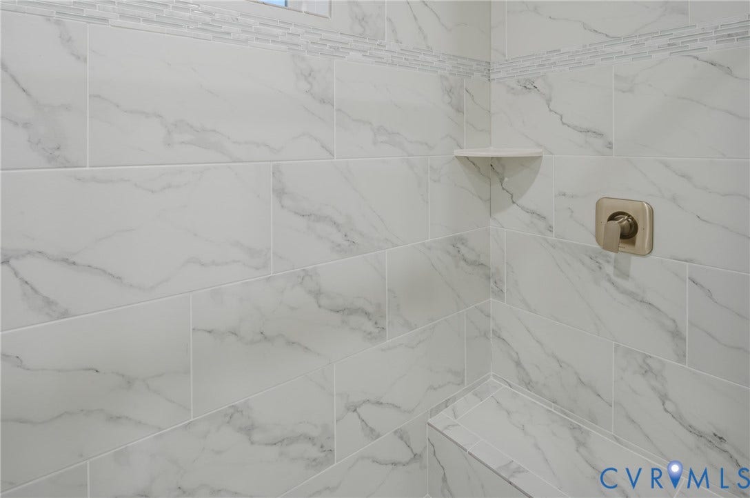 Tiled shower surround with a decorative accent band, built-in corner shelf, and a built-in shower bench
