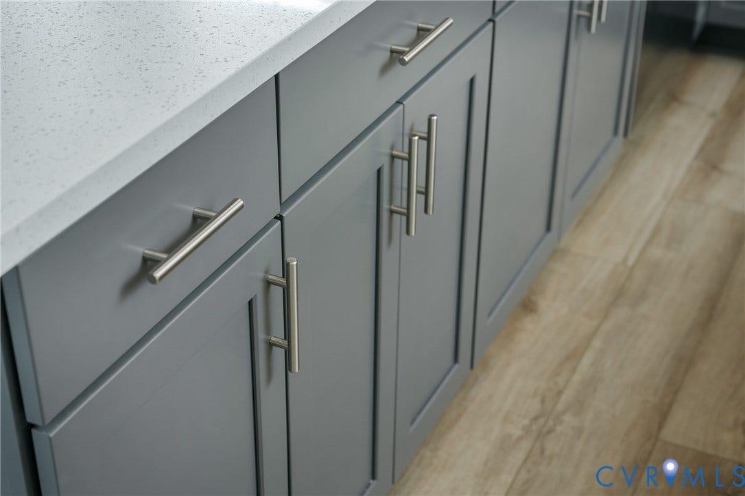 Gray shaker-style cabinetry with brushed nickel hardware, light-toned countertop, and wood-finish flooring