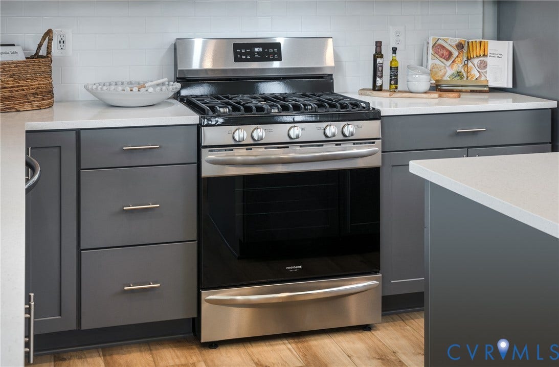 Stainless steel range, dark grey cabinetry, light-toned countertops, white subway tile backsplash, and wood-finish flooring