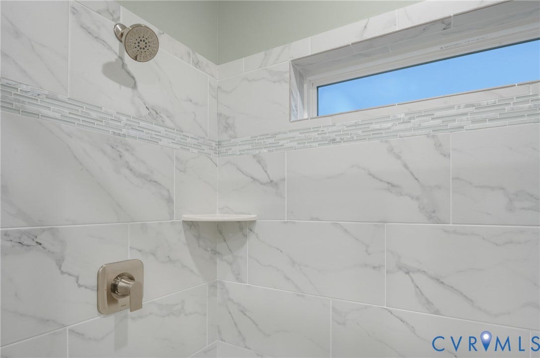 Shower with large format white tile featuring gray veining, a decorative glass tile accent band, and a built-in corner shelf