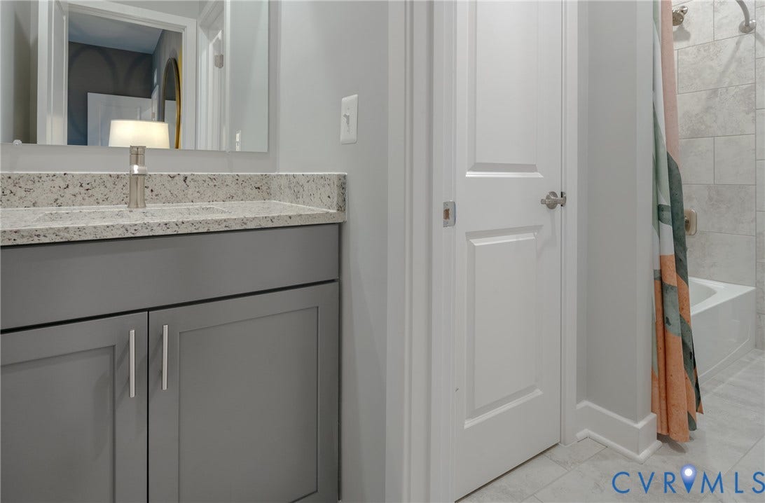 Bathroom featuring a gray vanity with a light-toned countertop, an undermount sink, a white tub, and tile flooring