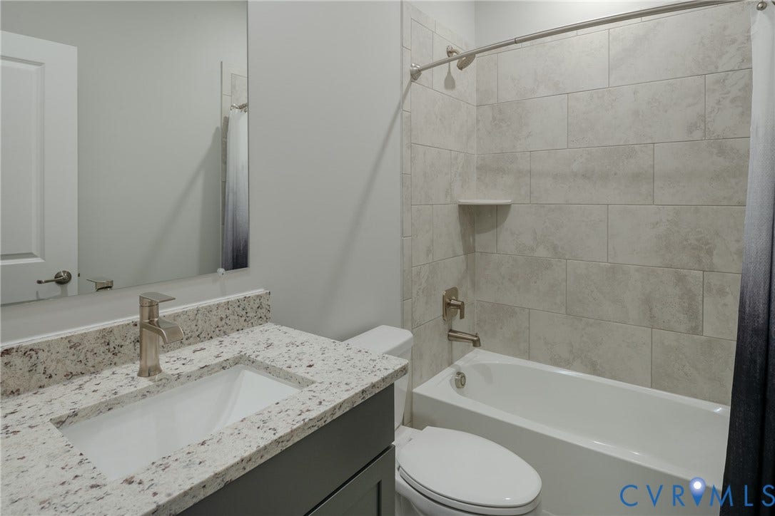 Integrated bathtub and shower with tiled surround, single vanity with light-toned countertop, and undermount sink