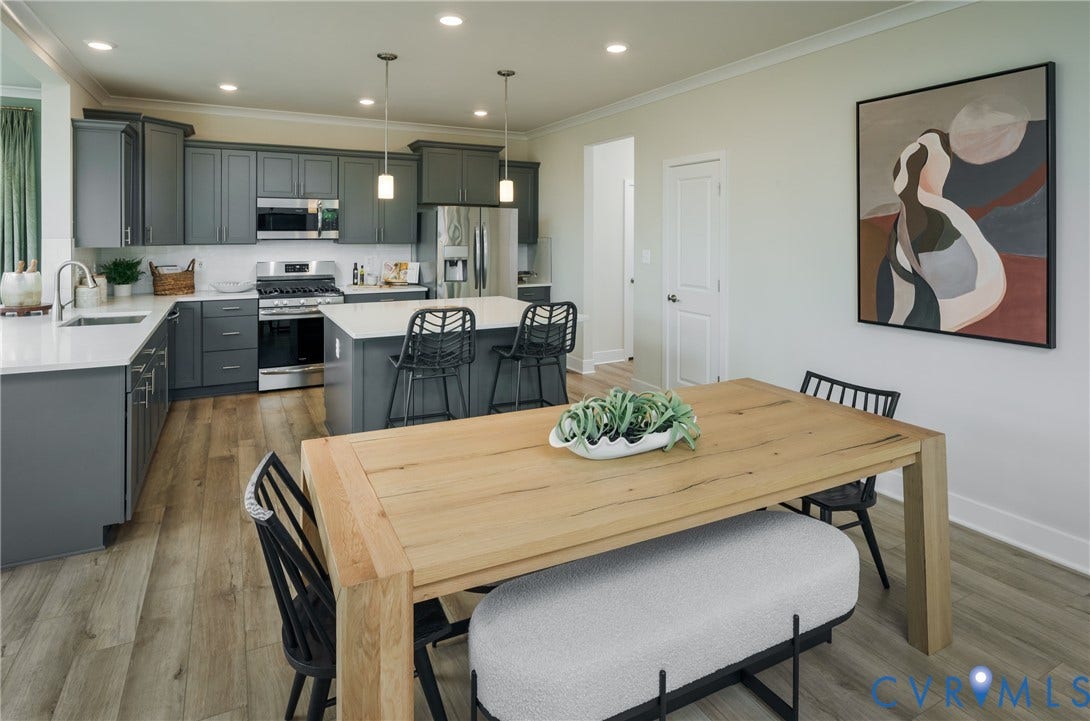 Open-concept dining and kitchen area featuring a wood-finish dining table, stainless steel appliances, gray cabinetry with white countertops, pendant lighting, and wood-finish flooring throughout the space