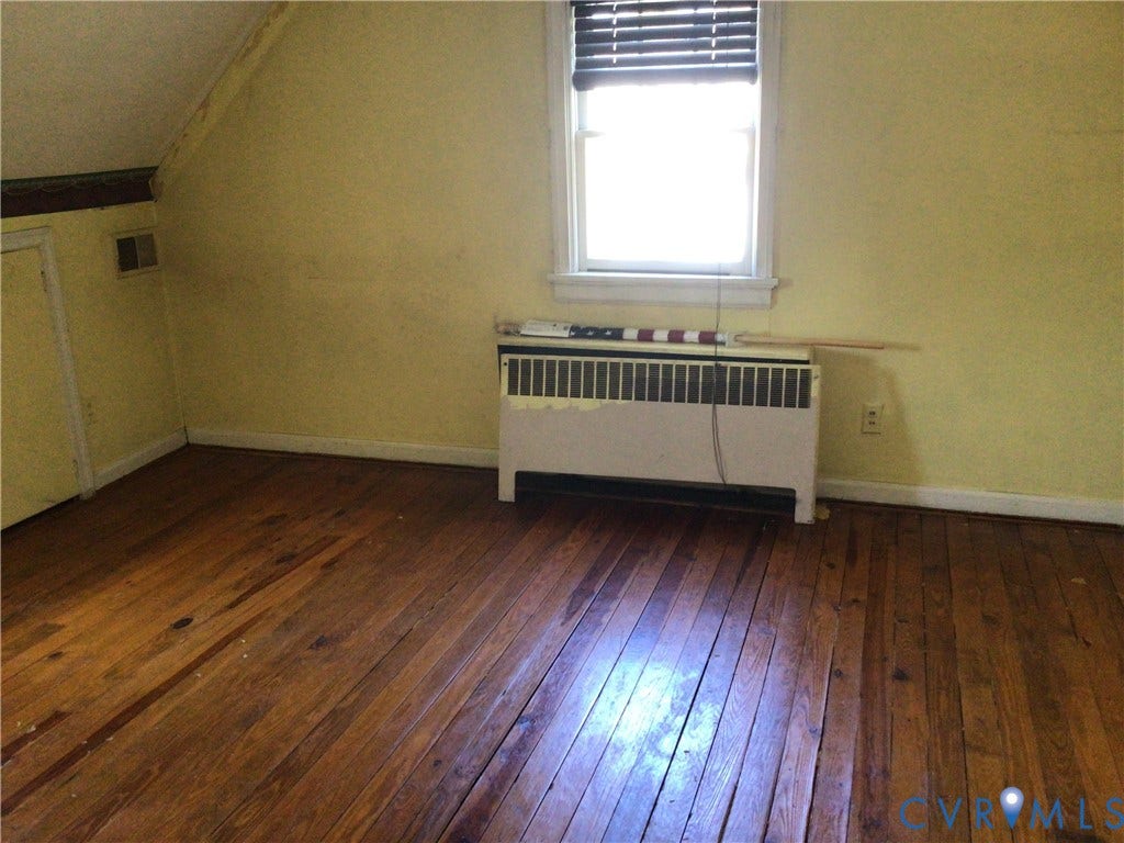 1307 Greystone Avenue, Richmond, VA 23224 Room interior featuring hardwood flooring, slanted ceiling, built-in floor-level heating unit, and a single-pane window with wood-frame trim