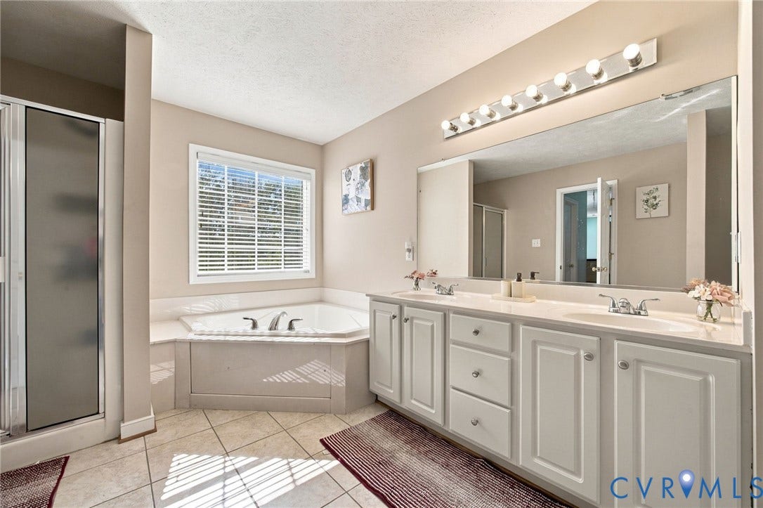 8119 Castle Grove Drive, Mechanicsville, VA 23111 Primary bathroom with Dual-sink vanity with white cabinetry, expansive wall-mounted mirror, corner soaking tub, and separate glass-enclosed shower