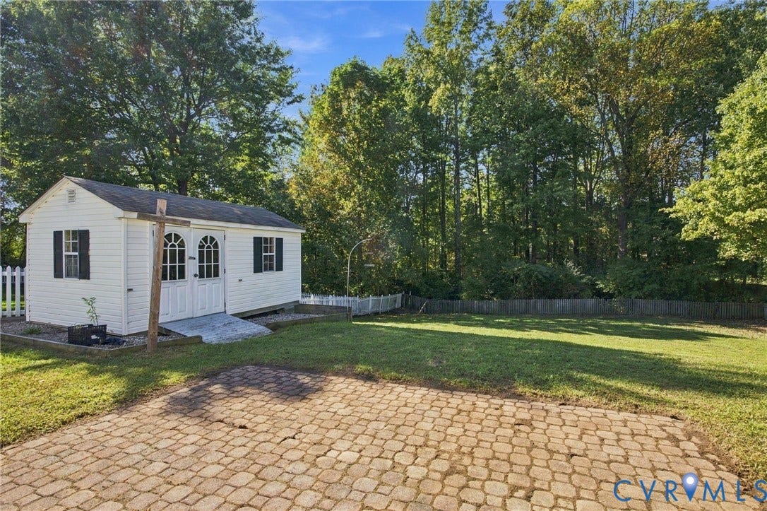 8119 Castle Grove Drive, Mechanicsville, VA 23111 Backyard featuring a paved stone patio, white vinyl picket fencing, and a detached outbuilding with double-door entry