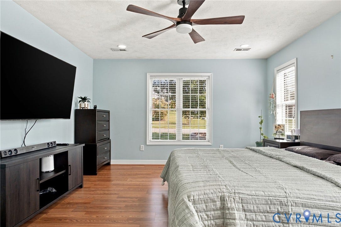 8119 Castle Grove Drive, Mechanicsville, VA 23111 Primary bedroom featuring wood-finish flooring, a multi-blade ceiling fan with integrated lighting, and dual windows equipped with white shutter blinds
