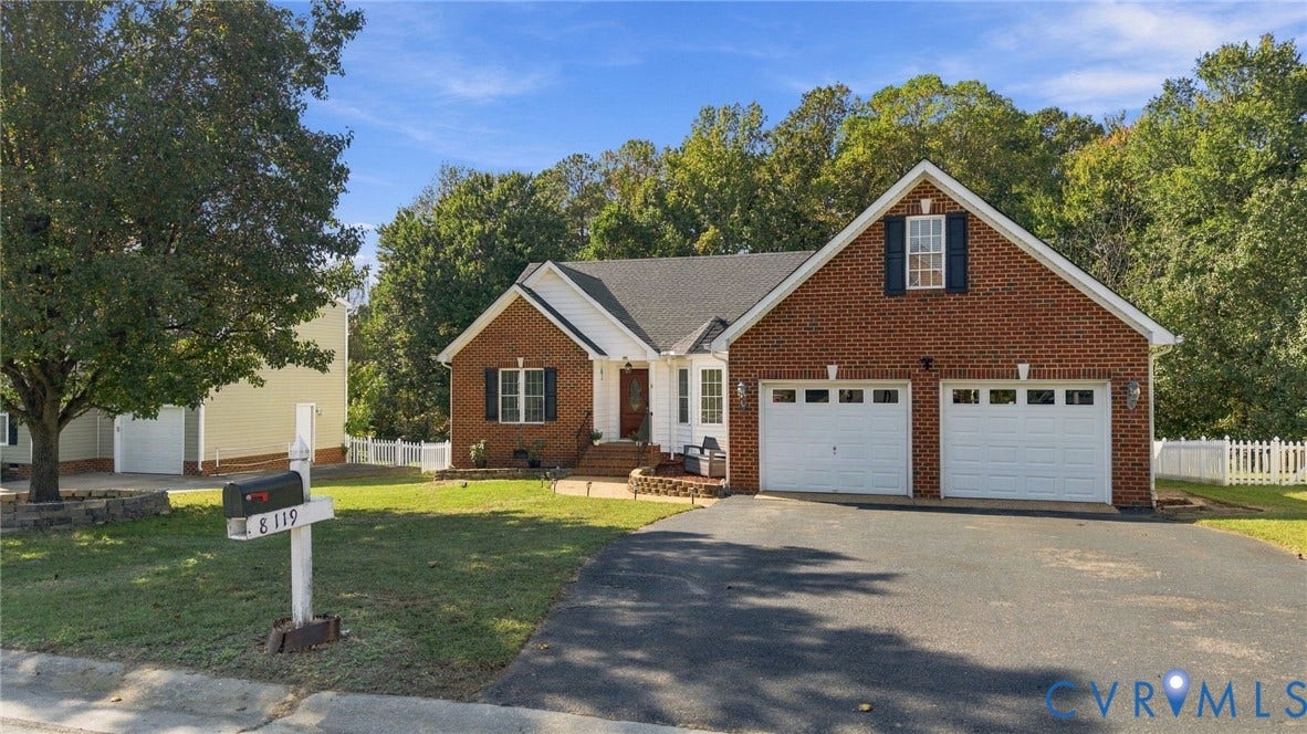 8119 Castle Grove Drive, Mechanicsville, VA 23111 Brick exterior featuring a two-car garage, asphalt driveway, covered entryway, and white picket fencing