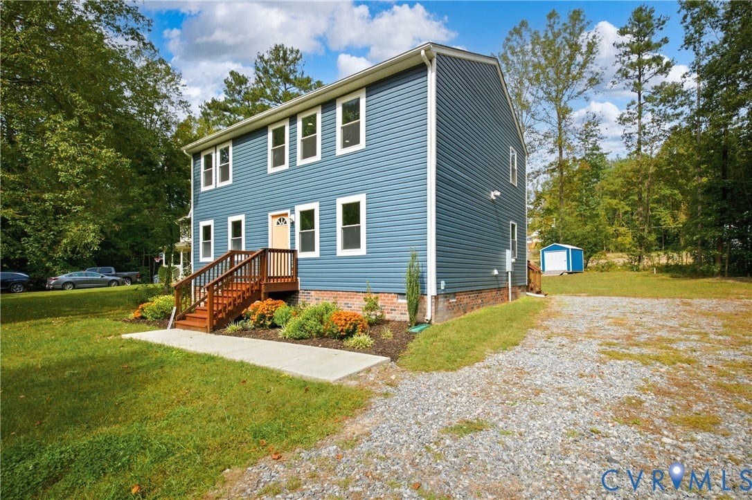 12089 Monterey Road, Ruther Glen, VA 22546 Two-story home with blue vinyl siding, brick foundation, wood-framed exterior staircase, concrete walkway, and gravel driveway