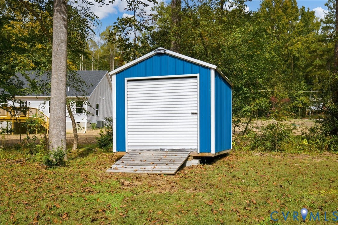 12089 Monterey Road, Ruther Glen, VA 22546 Detached storage structure featuring metal siding, a white roll-up door, and an integrated wood-slat ramp