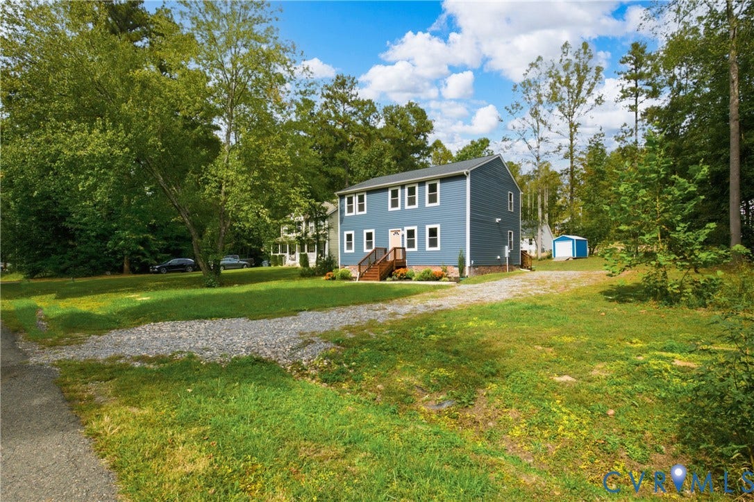 12089 Monterey Road, Ruther Glen, VA 22546 Two-story residence featuring blue horizontal siding, a gravel driveway, an elevated front wooden deck, and a detached storage structure on a tree-lined lot