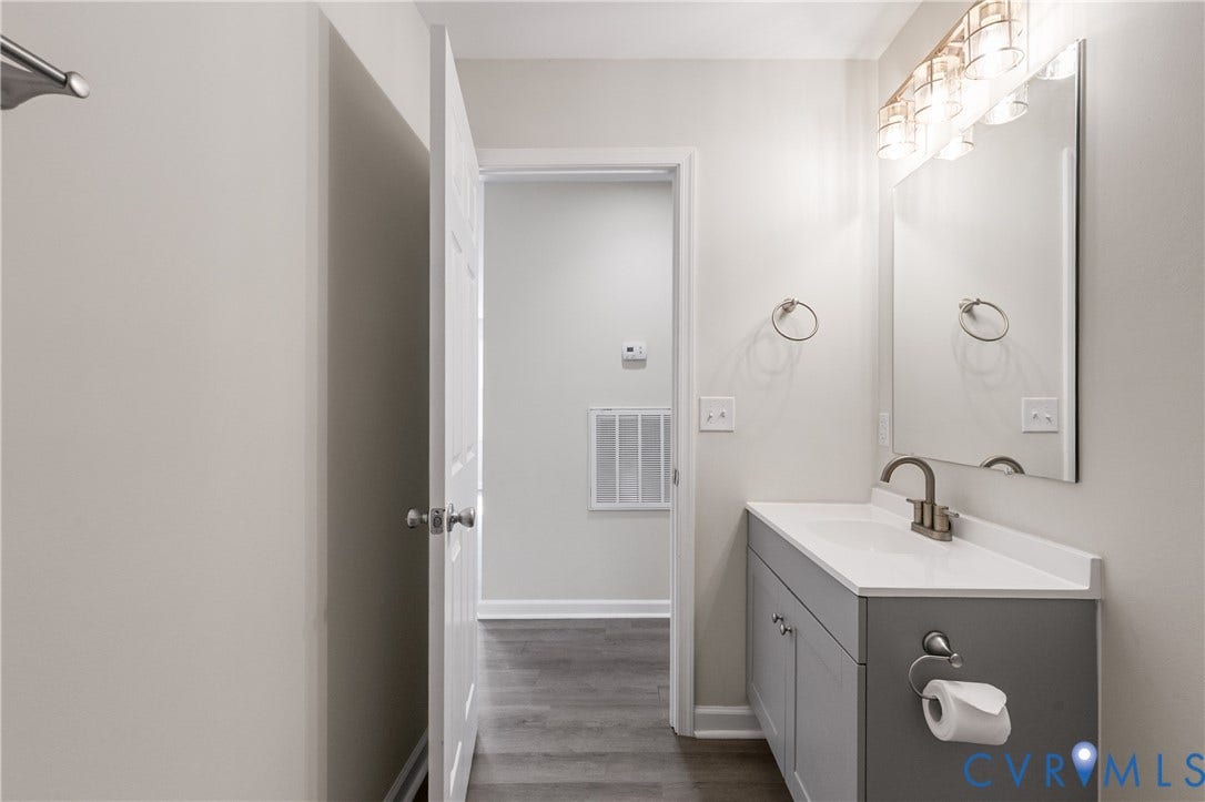 12089 Monterey Road, Ruther Glen, VA 22546 Grey vanity featuring a solid surface countertop, integrated sink, and brushed-finish faucet, accompanied by a rectangular wall-mounted mirror, multi-bulb vanity light fixture, and wood-finish flooring