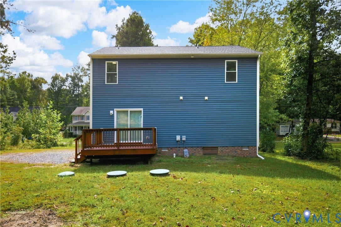 12089 Monterey Road, Ruther Glen, VA 22546 Rear exterior featuring blue horizontal siding, a raised wood deck, a brick foundation base, and a sliding glass door