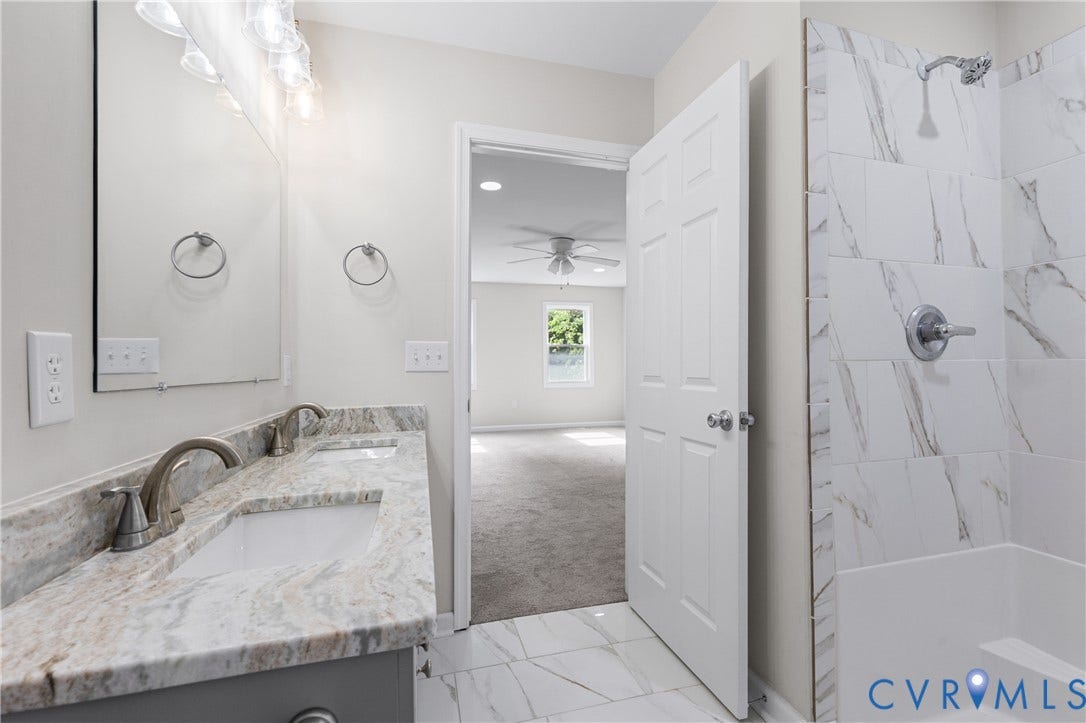 12089 Monterey Road, Ruther Glen, VA 22546 Bathroom featuring a dual-sink vanity with stone-finish countertop, undermount sinks, large wall-mounted mirror, and a shower-tub combination with tiled surround