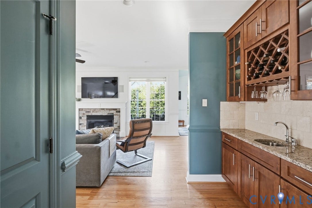 4502 Jennway Turn, Summer Lake, Moseley, VA 23120 Built-in wet bar featuring stone-surface countertops, custom wood cabinetry, integrated wine storage, and a stainless steel prep sink, complemented by wood-finish flooring and a fireplace with a stone-surround mantel