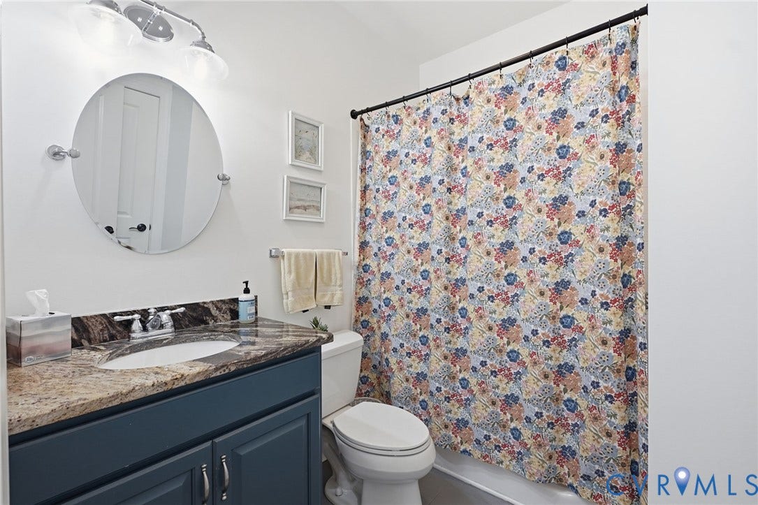 4502 Jennway Turn, Summer Lake, Moseley, VA 23120 Blue-toned vanity cabinet featuring a stone-look countertop, integrated oval sink, circular wall-mounted mirror, and three-light overhead fixture