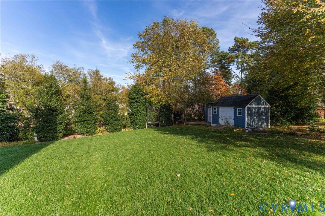 4502 Jennway Turn, Summer Lake, Moseley, VA 23120 Expansive lawn area featuring mature trees, peripheral evergreen hedging, and a detached storage structure with a shingled roof