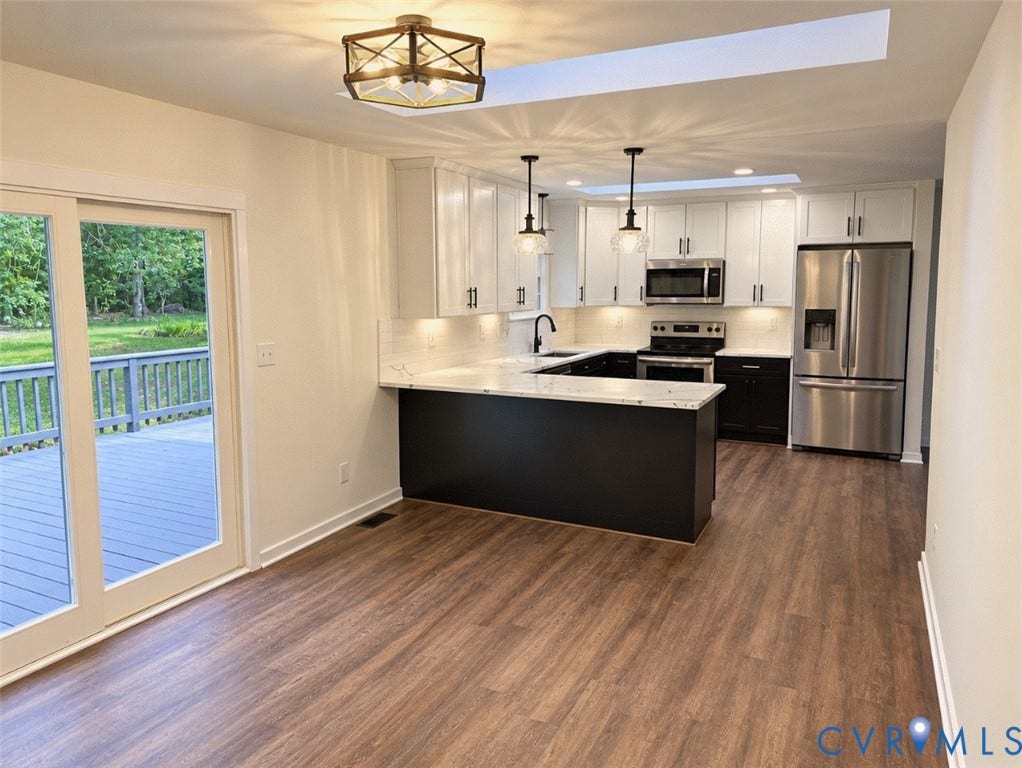 Modern kitchen featuring stainless steel appliances, white cabinetry, dark island base, and wood-finish flooring