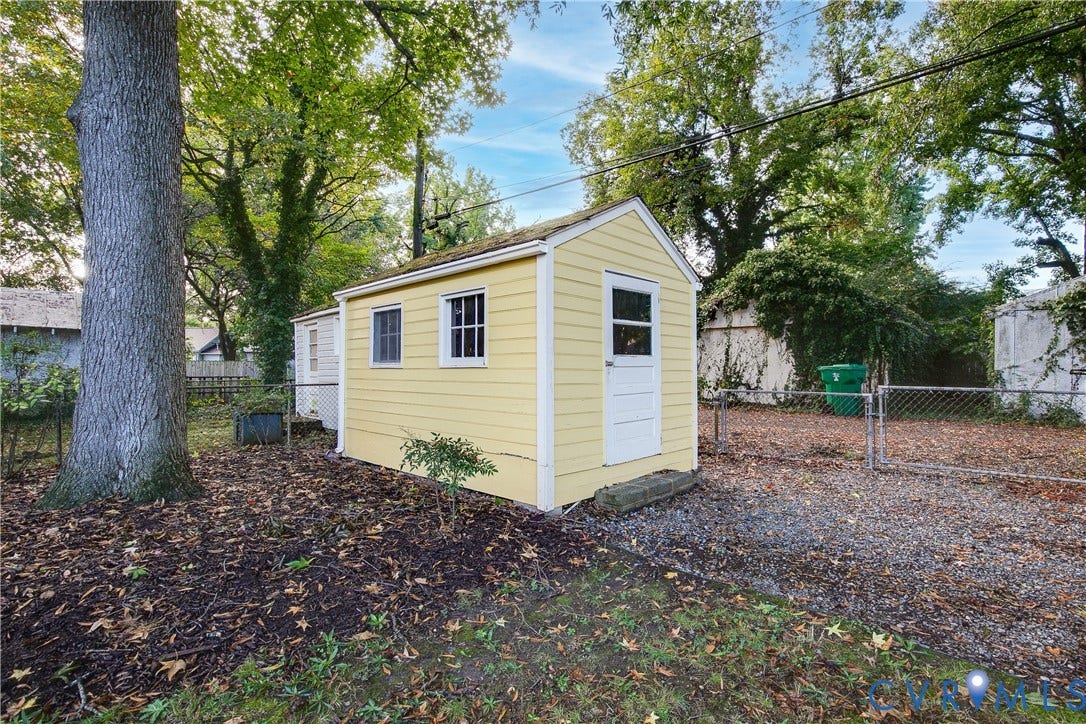 3006 Porter Street, Richmond, VA 23225 Detached storage structure featuring yellow horizontal siding, a single-entry door, and two multi-pane windows, set within a lot enclosed by chain-link fencing