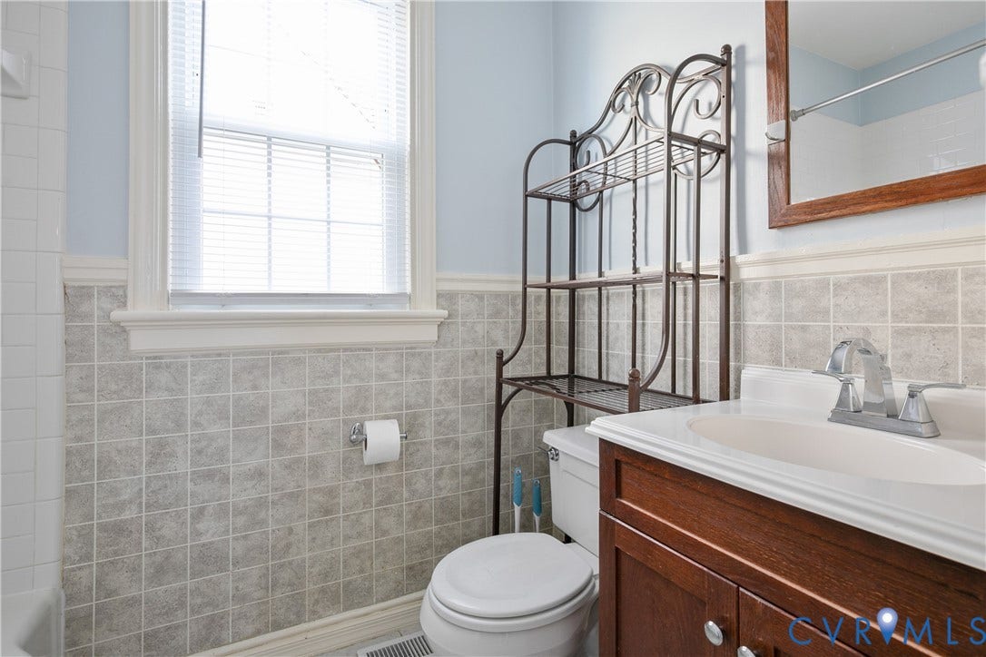 3006 Porter Street, Richmond, VA 23225 Vanity with wood-finish cabinetry, neutral countertop, rectangular basin, chrome widespread faucet, and half-height tile wainscoting