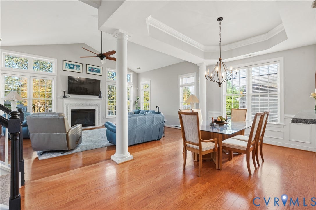3360 Manor Grove Circle, Glen Allen, VA 23059 Open-concept living space featuring wood-finish flooring, vaulted ceilings with recessed tray detailing, a central decorative column, fireplace with white mantle, and oversized windows