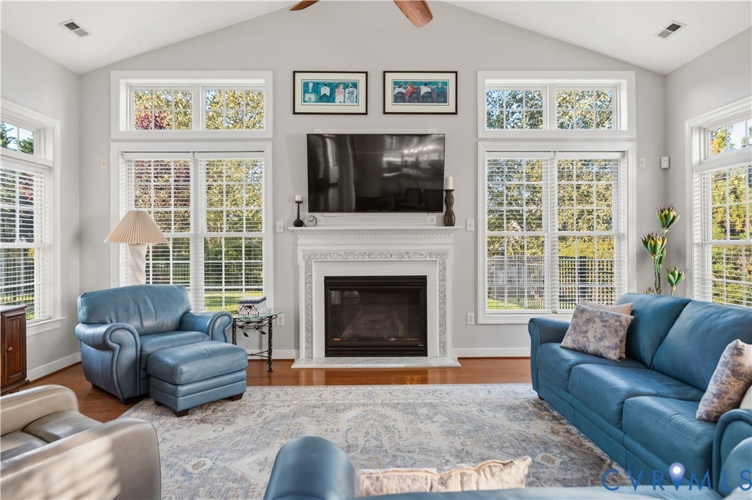 3360 Manor Grove Circle, Glen Allen, VA 23059 Vaulted ceiling with a central fan, fireplace with detailed millwork surround, expansive windows with grid muntins, and polished wood-finish flooring