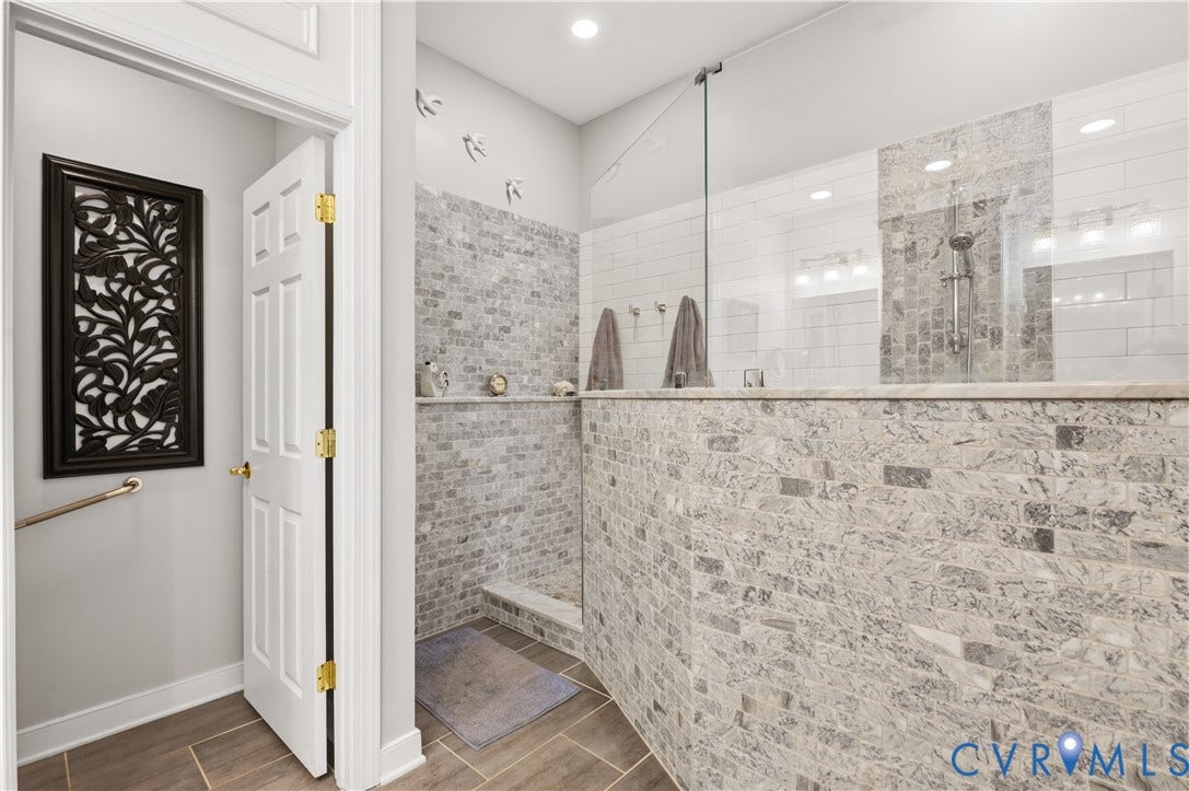 3360 Manor Grove Circle, Glen Allen, VA 23059 Walk-in shower featuring textured stone tile wall cladding, a frameless glass partition, white subway-style tile accents, and a rainfall shower head