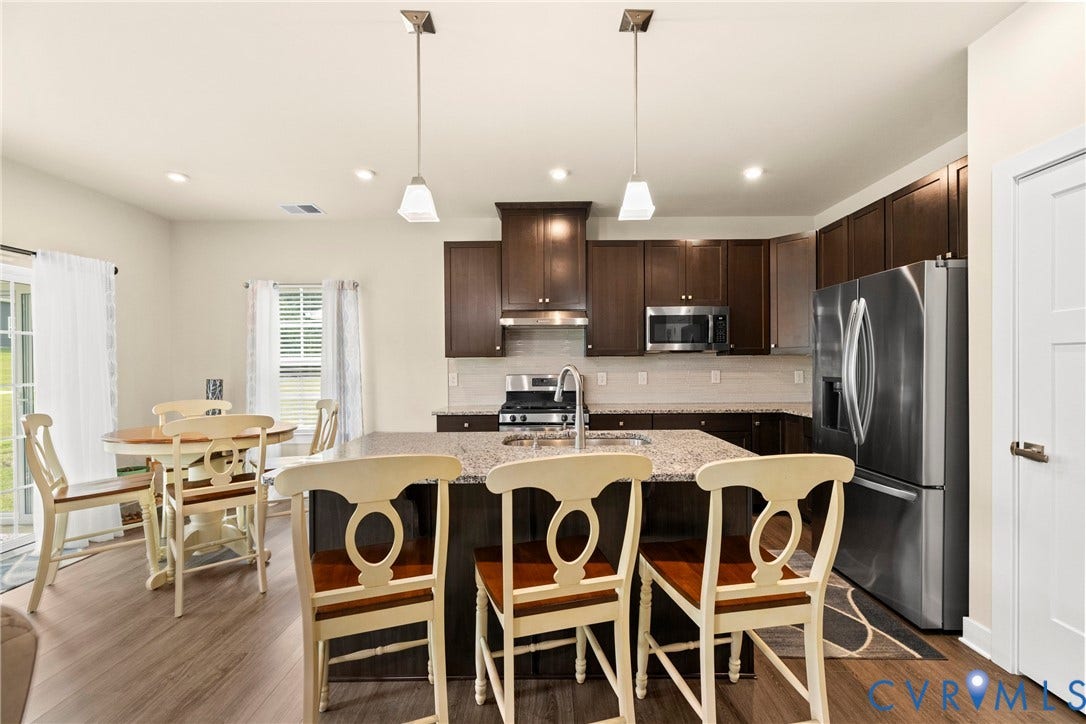 Kitchen featuring dark-finish cabinetry, stone-surface center island with integrated sink, stainless steel appliances, wood-finish flooring, and dual hanging pendant lights