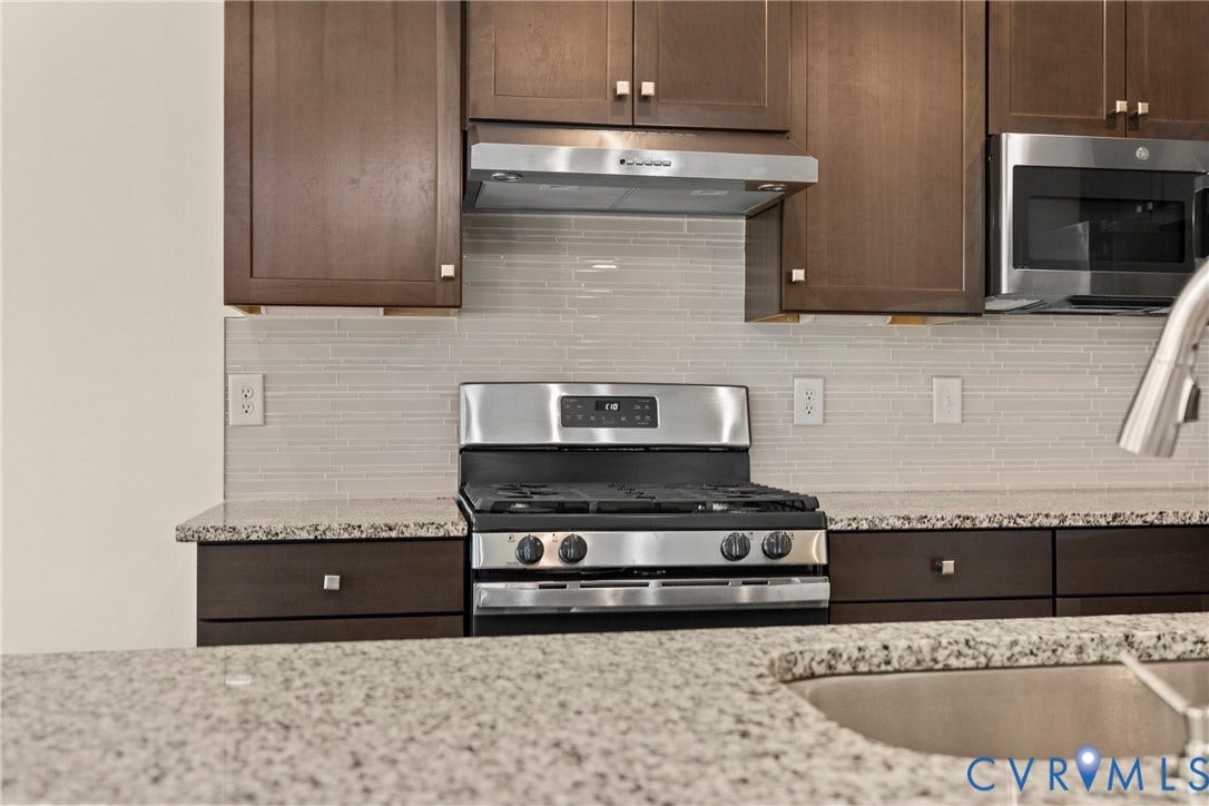 Kitchen featuring dark-finish cabinetry, stone-surface countertops, stainless steel appliances, and a horizontal linear-tile backsplash