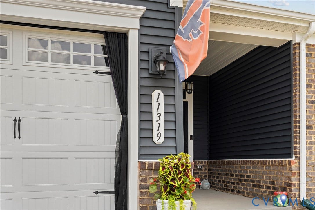 Exterior featuring dark horizontal siding, brick masonry detailing, a paneled garage door with transom windows, and a covered entryway