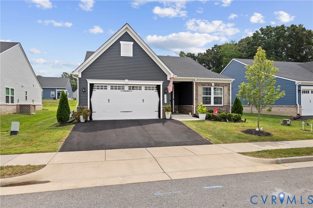 Single-story exterior featuring dark lap siding, brick masonry detailing, a two-car garage, and an asphalt driveway