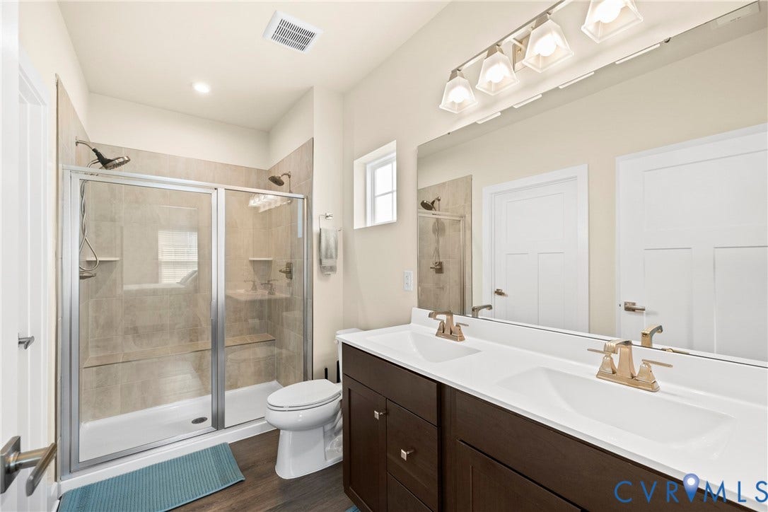 Double vanity with rectangular sinks, white countertop, dark cabinetry, full-width mirror, and walk-in shower with tile surround