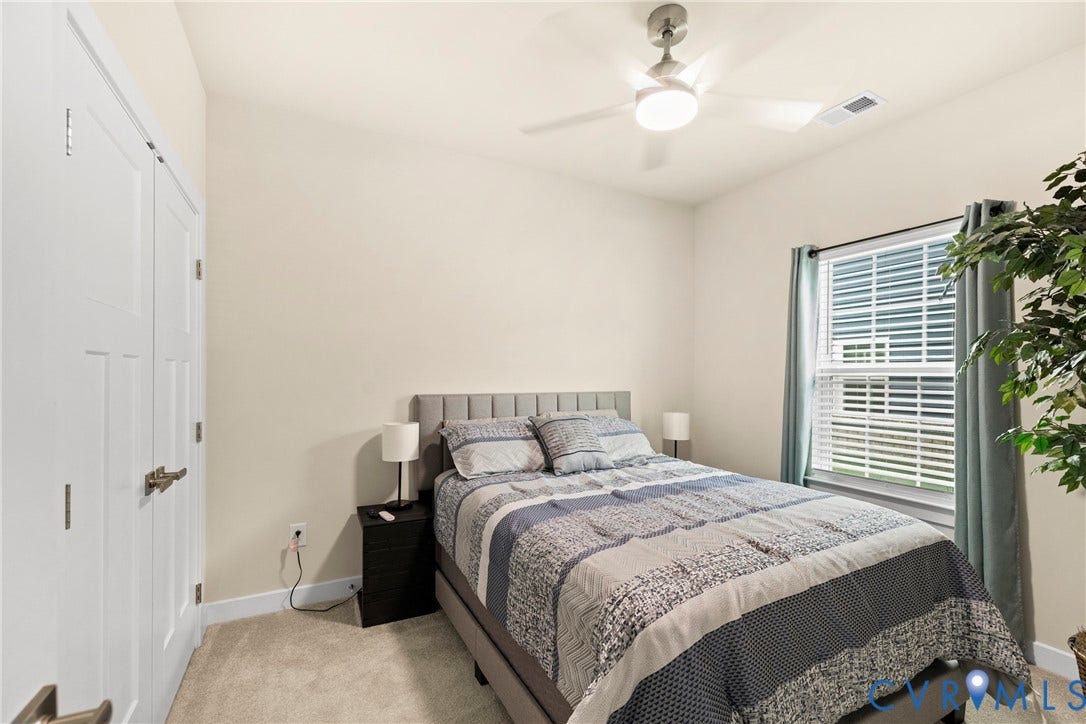Neutral-toned interior featuring wall-to-wall carpeting, dual-panel closet doors, and a ceiling-mounted light fixture with integrated fan