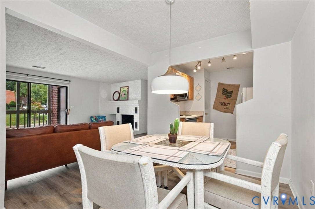 Open-concept area featuring wood-finish flooring, a white-painted brick fireplace, a metal pendant light fixture, and large sliding glass doors