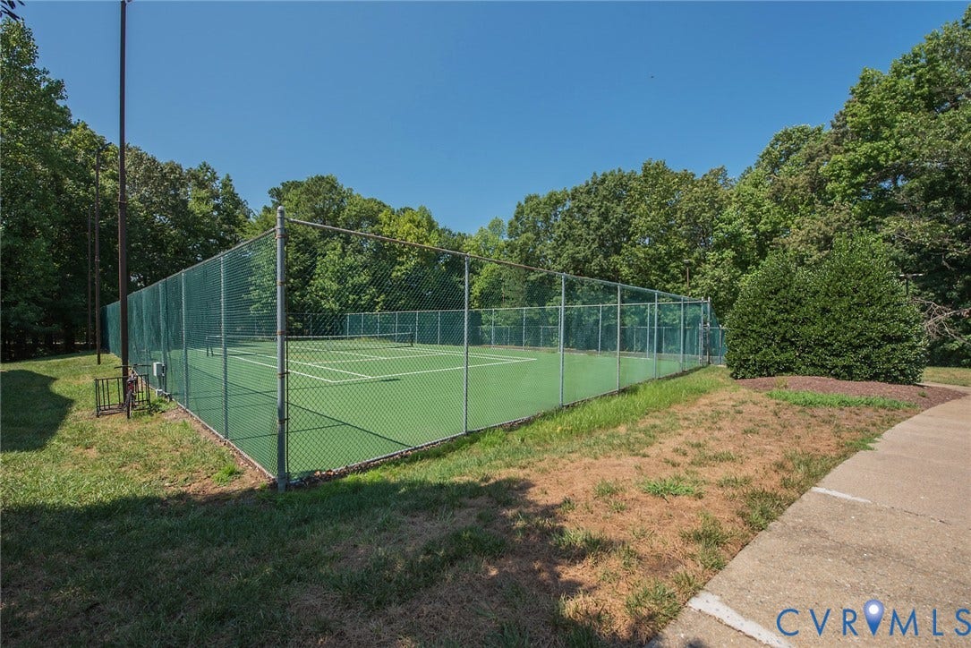 Tennis court featuring a perimeter chain-link fence, hard court surface, and concrete walkway