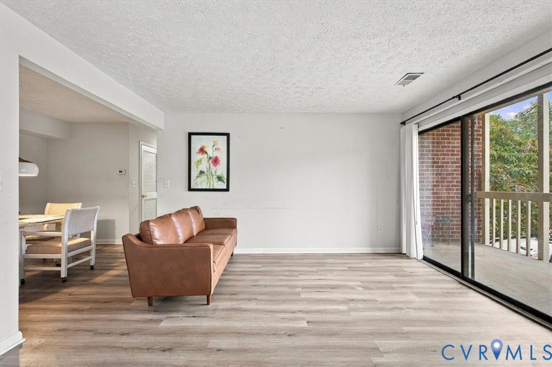 Living area featuring wood-finish flooring and a large sliding glass door providing access to a covered balcony with a brick exterior finish