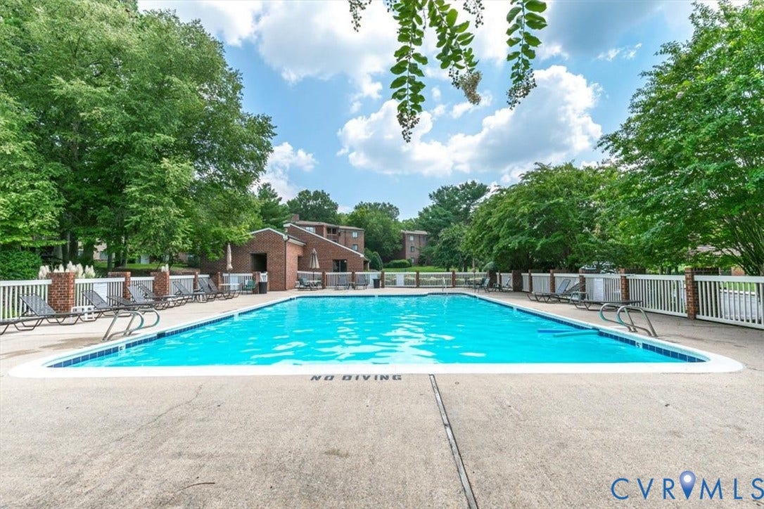 Outdoor swimming pool featuring a concrete deck, white perimeter fencing, and brick pillars