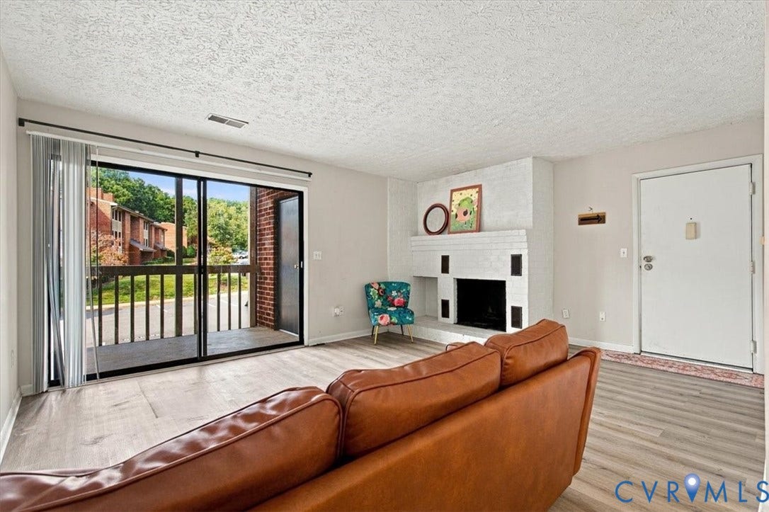 White painted brick fireplace, wood-finish flooring, and sliding glass door with balcony access