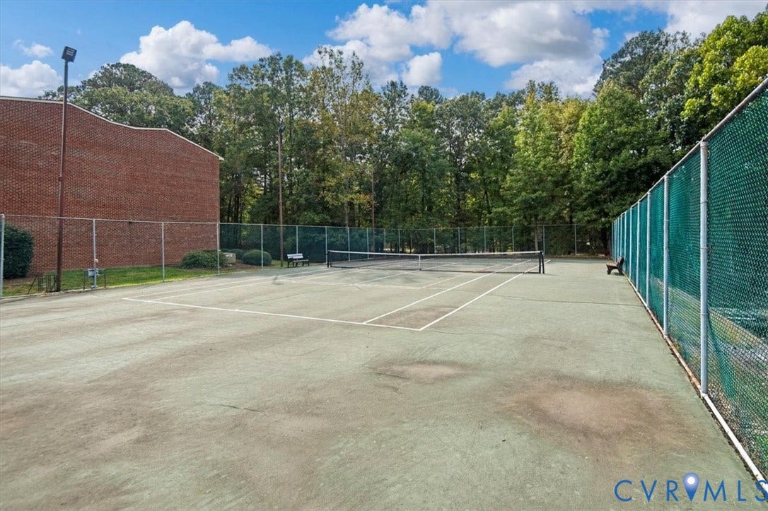 Tennis court featuring a hard surface, perimeter chain-link fencing, and built-in benches