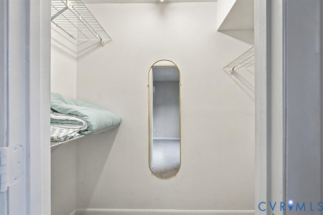 Walk-in storage space featuring dual-tier metal wire shelving and a pill-shaped wall-mounted mirror with a metallic frame