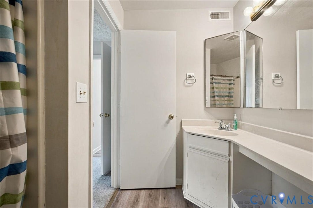 Bathroom featuring a vanity with an integrated countertop, tri-fold medicine cabinet, wood-finish flooring, and multi-bulb vanity lighting