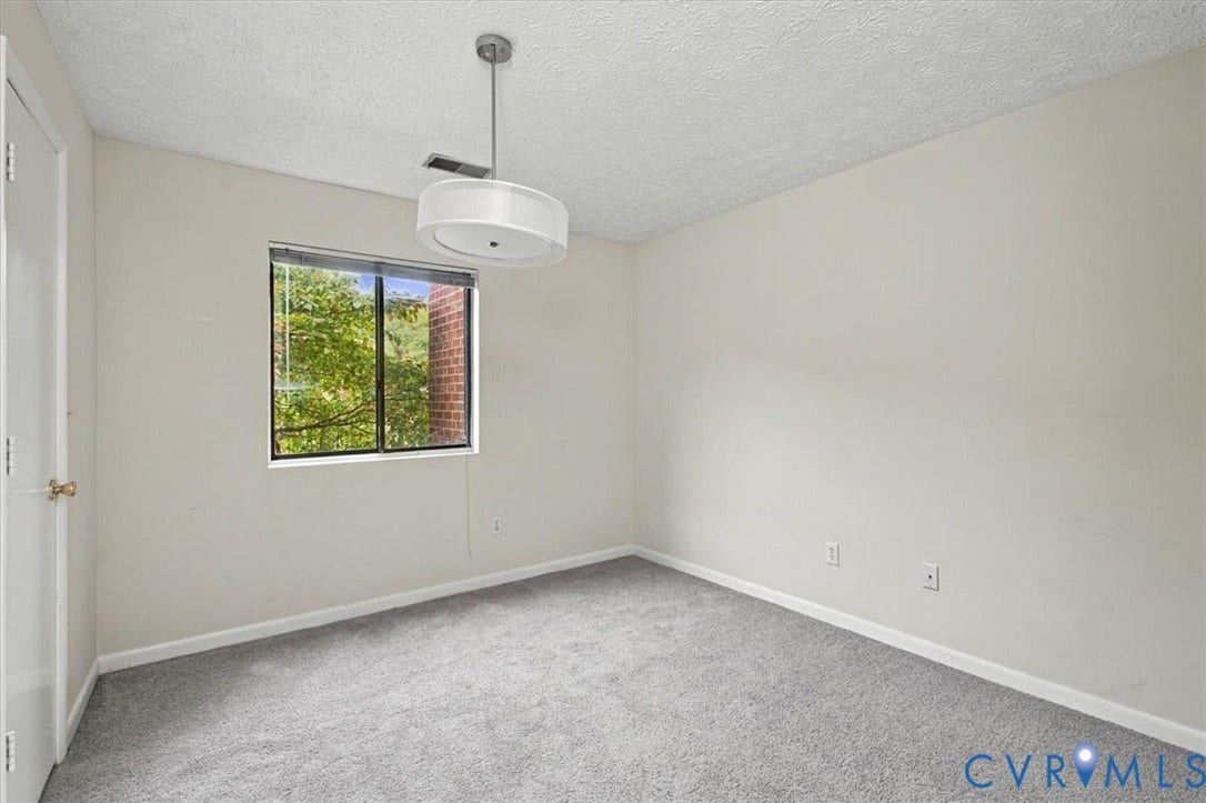 Neutral-toned carpeted room featuring a white drum pendant light fixture and a single-pane window