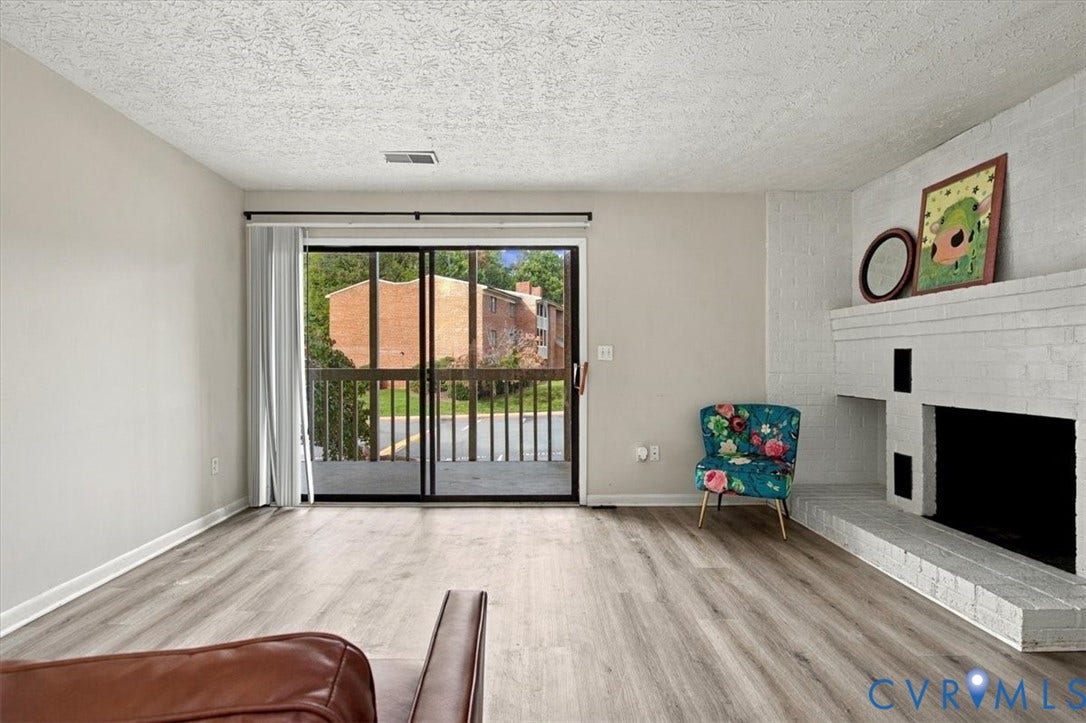 Painted brick fireplace with a raised hearth, wood-finish flooring, and sliding glass door with access to a balcony
