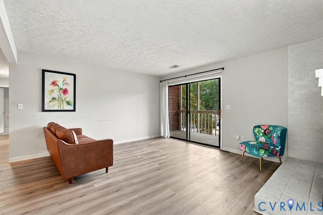 Living area featuring wood-finish flooring, a painted brick fireplace, and sliding glass doors leading to an exterior deck