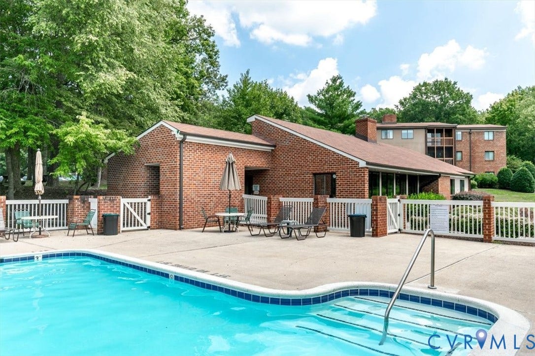 Outdoor swimming pool with concrete decking, white picket fencing, and brick clubhouse exterior