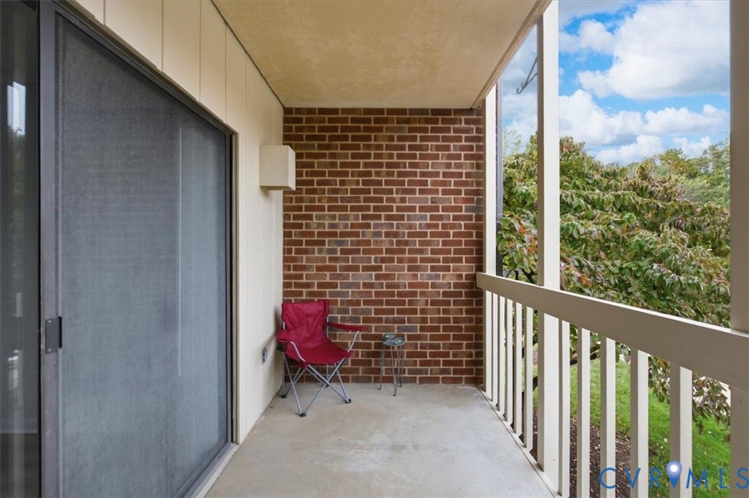 Covered balcony featuring a red brick accent wall, concrete flooring, and a vertical balustrade railing