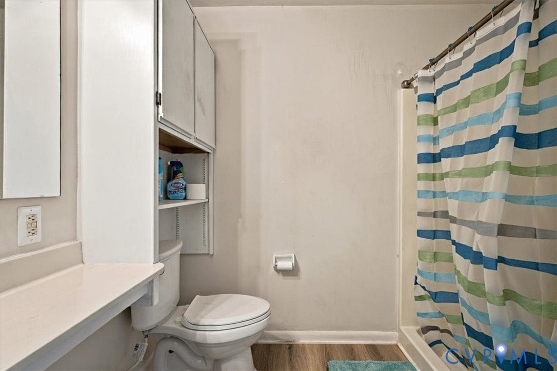 Bathroom featuring wood-finish flooring, a white vanity with integrated surface, wall-mounted upper cabinetry, and a shower-tub combination